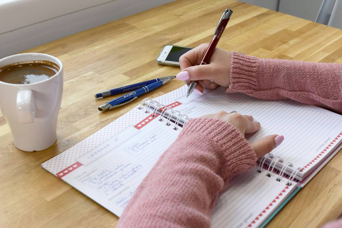 A person journaling beside a stack of books with quotes on self development and growth written on sticky notes